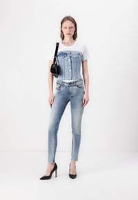 Jeans korzet s gumbima preko bijele majice, u kombinaciji s izblijedjelim plavim uskim trapericama i crnim visokim potpeticama; mali crni ručni torbica kao akcent.