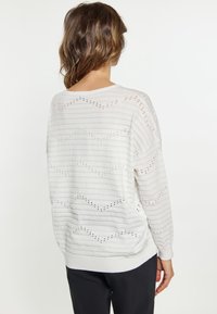 Lichte gebreide trui in off-white, met horizontale strepen en kleine gaatjespatronen. Ontspannen pasvorm met ribbels aan de mouwen en onderkant.
