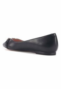 Bailarina de piel negra con punta redondeada, un pequeño detalle de lazo y una textura suave. Suela baja y plana con mínimos acentos.