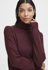 Burgundy turtleneck neule, jossa on ribbed hihansuut, pehmeä rakenne ja rento istuvuus. Kangas näyttää kevyeltä ja mukavalta.