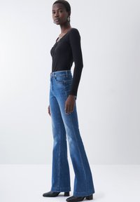 Jeans a zampa d'elefante in denim blu, con vita alta e tasche frontali, abbinati a un top a maniche lunghe nero a coste. Tessuto liscio, design aderente.