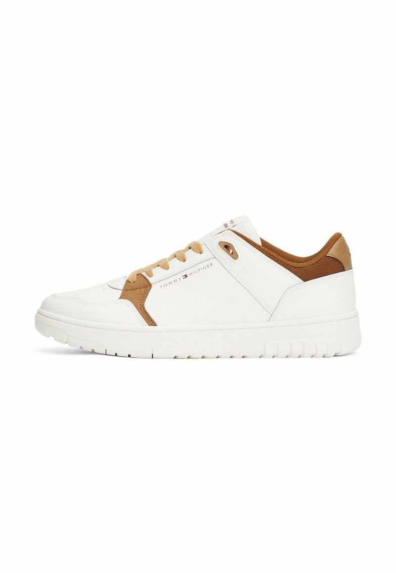 Sneaker blanche avec des accents beiges, présentant une tige texturée, un embout rond et un système de laçage. Logo imprimé sur le côté et semelle en caoutchouc.