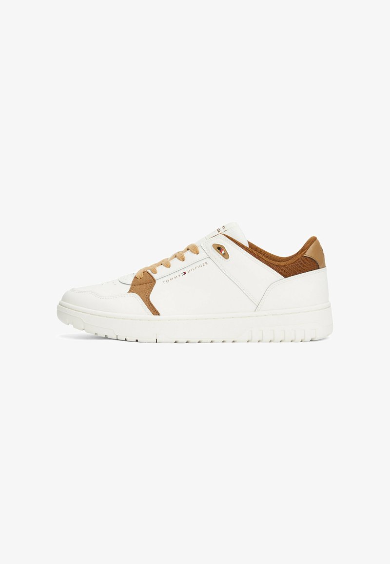 Sneaker blanche avec des accents beiges, présentant une tige texturée, un embout rond et un système de laçage. Logo imprimé sur le côté et semelle en caoutchouc.