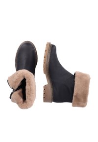 Bottines en cuir noir avec une doublure en fourrure beige, présentant une surface texturée et une semelle en caoutchouc striée. Fermeture éclair sur le côté.