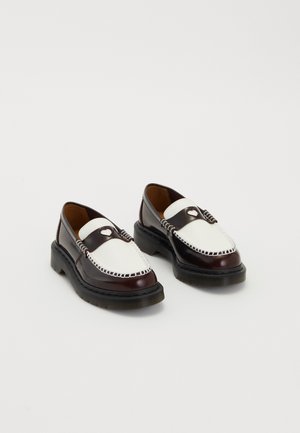 Um par de mocassins de couro bicolor em tons de castanho e branco, com detalhes de costura e solas grossas pretas, sobre um fundo simples.