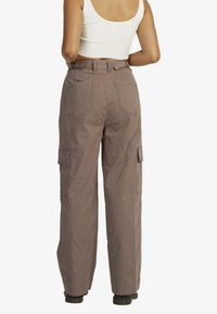 Cargo pants in a muted taupe color, made from sturdy fabric, featuring a relaxed fit, side pockets, and back pockets with a subtle stitch detail.