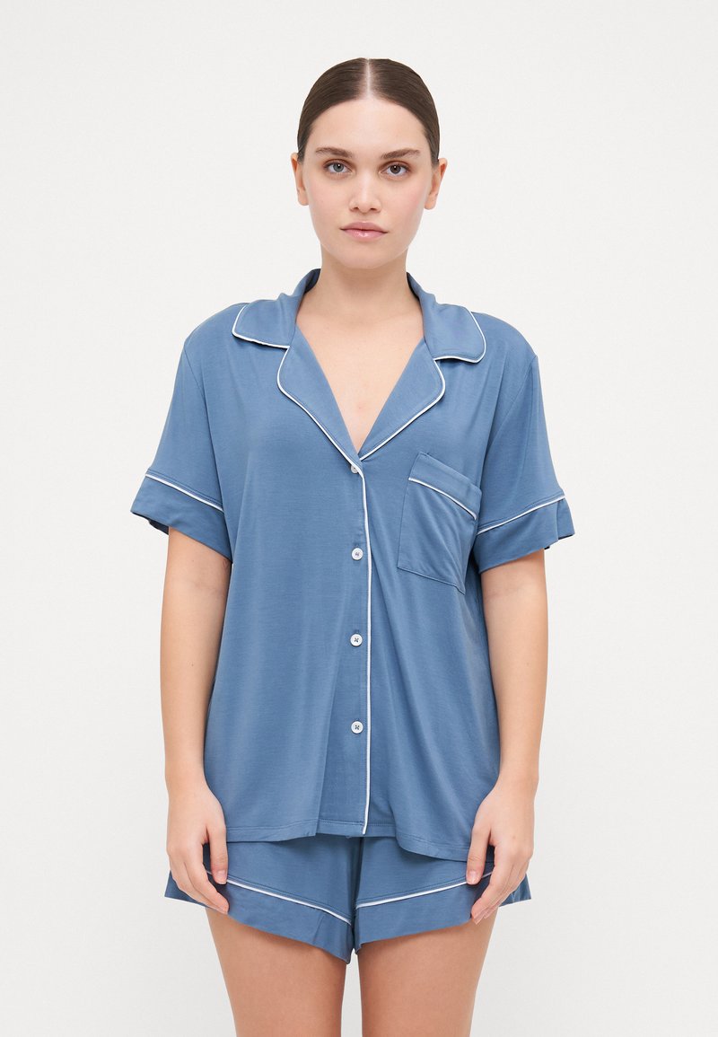 Conjunto de pijama de manga curta azul, feito de um tecido suave e respirável. A parte de cima apresenta uma frente com botões, colarinho e um único bolso no peito.