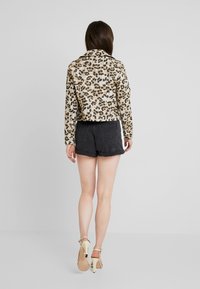 Kurtka w panterkę wykonana z teksturowanej tkaniny, z kołnierzem i dopasowanym krojem, zestawiona z czarnymi szortami dżinsowymi i jasnymi szpilkami.