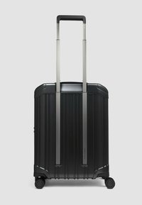 Valigia nera rigida con scanalature verticali, due maniglie retrattili argento e quattro ruote nere per la mobilità. Design compatto e strutturato.