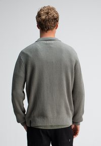 Grijze geribbelde gebreide trui met een opgerolde kraag en lange mouwen, voorzien van een gestructureerd patroon en een rechte zoom.