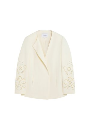 Blazer de color crema a medida con solapas con muescas y patrones decorativos de tachuelas doradas y plateadas en las mangas.