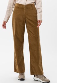 Bruna kordflorsbyxor med vida ben och knappstängning, med vertikal ribbtextur. Parat med ljusa sneakers.