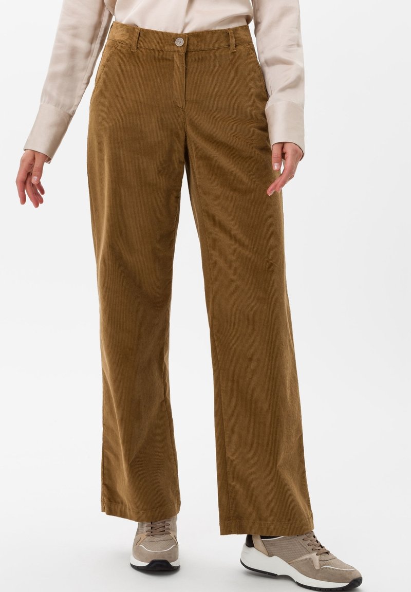 Bruna kordflorsbyxor med vida ben och knappstängning, med vertikal ribbtextur. Parat med ljusa sneakers.