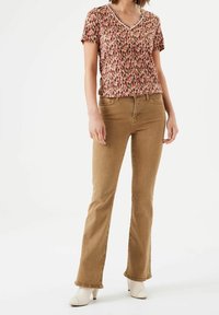 Blůza s krátkým rukávem s květinovým vzorem v růžové a hnědé barvě, spárovaná s světle hnědými zvonovými džíny a bílými sandály na podpatku.