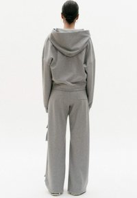 Szara bluza z kapturem i pasujące spodnie wykonane z miękkiego materiału. Spodnie mają boczne falbany i luźny krój. Minimalistyczny design bez wzorów.