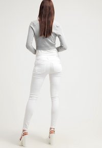 Šedý zkrácený svetr, bílé skinny džíny a bílé platformové sandály. Obsahuje přiléhavý design, žebrovanou texturu na svetru a zadní kapsy.