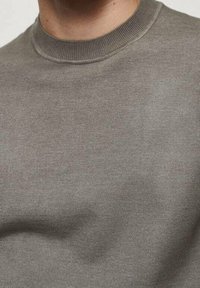 Suéter gris de cuello redondo hecho de un tejido suave. Presenta un cuello acanalado y un diseño minimalista con una textura lisa.