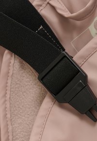 Sangle noire ajustable avec une boucle carrée sur un tissu rose présentant une texture intérieure douce et des bords cousus.