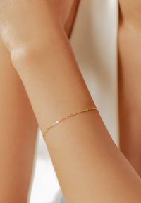 Pulsera de oro con un diseño de cadena delicada, con pequeños motivos de estrellas, llevada en una muñeca de tono de piel suave, destacando su estilo minimalista.