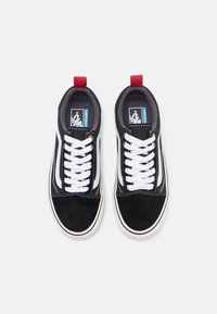 Zapatillas negras con cordones blancos, punta de gamuza y franjas laterales blancas en contraste. Incluye una lengüeta roja y un acolchado en el tobillo.