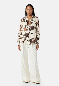 Lange mouw blouse in crème met bruin en zwart spetterprint, knoopsluiting aan de voorkant, klassieke kraag, lichtgewicht stof, getailleerde pasvorm.