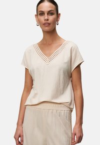 Maglietta beige chiara a V con maniche corte, con bordo testurizzato lungo il collo e un taglio ampio per il comfort.