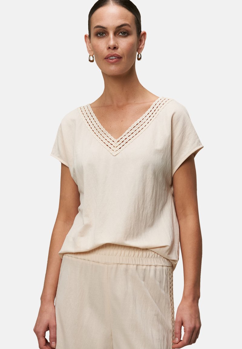 Maglietta beige chiara a V con maniche corte, con bordo testurizzato lungo il collo e un taglio ampio per il comfort.