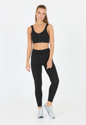 Soutien-gorge de sport noir avec une fermeture éclair à l'avant, associé à un legging noir taille haute. Tissu lisse, design ajusté, avec des détails de couture subtils.