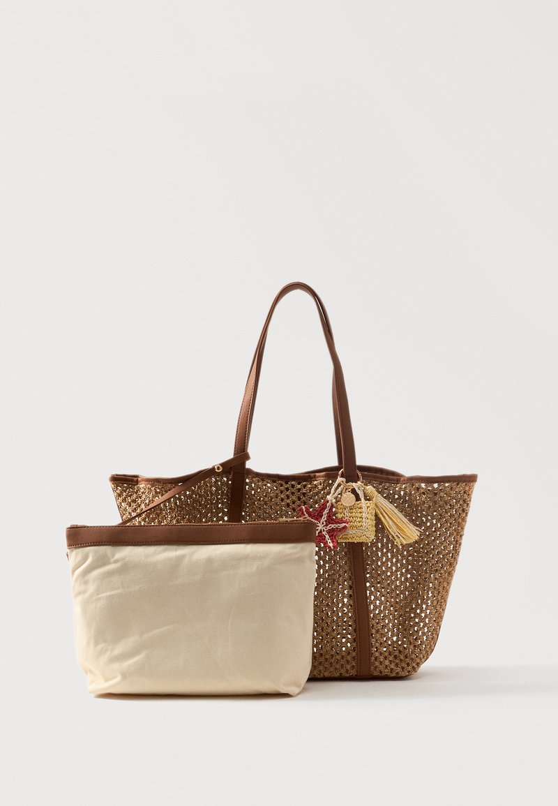 Sac fourre-tout tressé marron avec poignées en cuir, décoré de petits pompons, et une pochette en tissu beige séparée avec une bordure marron à l'avant.