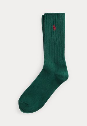 Chaussette en vert foncé côtelée avec logo de polo brodé en rouge, longueur mi-mollet, pliée soigneusement sur fond blanc.