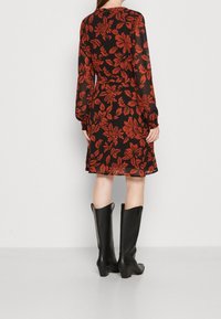 Vestido negro con estampado floral rojo, mangas largas, cintura ceñida y falda acampanada, combinado con botas negras de cuero hasta la rodilla.