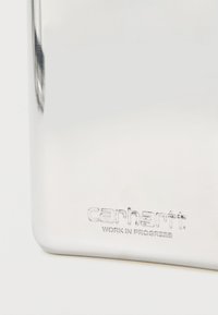 Gros plan sur une surface métallique argentée brillante avec l'inscription "carhartt WORK IN PROGRESS" gravée près du bord inférieur.