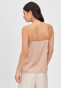 Camisola de seda nua com alças finas ajustáveis, textura suave e um corte relaxado, combinada com calças leves e fluidas.