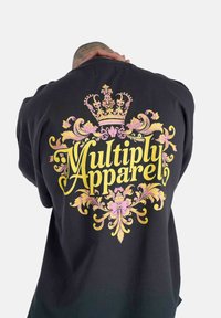 Sudadera negra con un diseño colorido que presenta una corona y el texto "Multiply Apparel" en amarillo y rosa, con acentos florales.