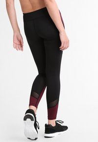 Black leggings with maroon accents and mesh panels, featuring a high waistband and tapered fit, designed for comfort and flexibility.