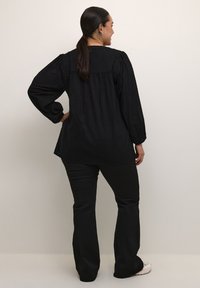 Blusa nera textured con maniche a sbuffo, polsini abbottonati e una vestibilità ampia. Abbinata a pantaloni neri a zampa d'elefante e sneaker bianche.