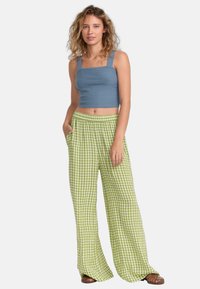 Svetlofialový rebrovaný crop top so štvorcovým výstrihom v kombinácii s širokými nohavicami s vzorom zeleno-bielej kárované. Model stojí s rukami v vreckách.