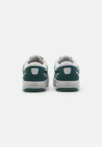 Sneaker in suede verde e tessuto bianco con suole in gomma grigia, caratterizzate da un logo prominente sul tallone e un collare imbottito.