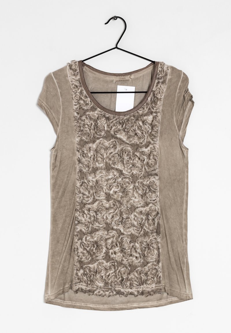 Chemise beige à manches courtes avec motif floral texturé sur le devant, encolure ronde, suspendue sur un cintre en fil noir avec une étiquette blanche à l'intérieur du col.