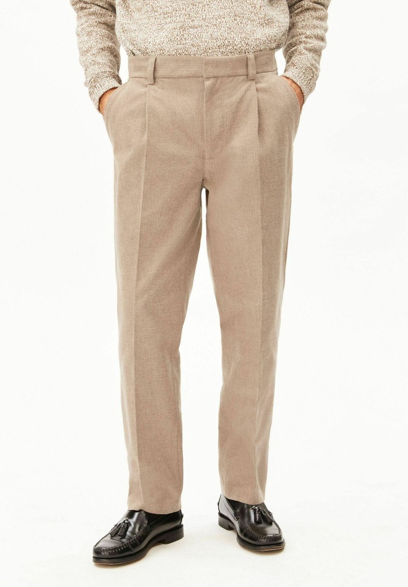 Beige corduroy trousers worn with hands in pockets and paired with black leather tassel loafers on a white background.