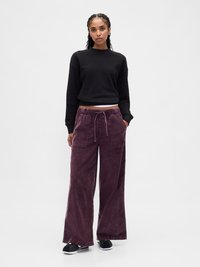 Μαύρο κοντό φούτερ συνδυασμένο με φαρδιά παντελόνια από βελούδο κοτλέ σε σκούρο μωβ. Τα παντελόνια διαθέτουν κορδόνι στη μέση και δύο εμπρόσθιες τσέπες. Μαύρα παπούτσια χωρίς κορδόνια.