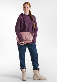 Suéter de punto morado con capucha, combinado con pantalones vaqueros azules y botas beige. Lleva un bolso acolchado rosa bajo el brazo.