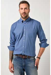 Camisa azul abotonada con un pequeño bolsillo en el pecho, mangas largas remangadas, combinada con jeans de mezclilla y un cinturón marrón. Textura de tela suave.