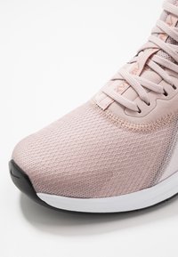 Lichtroze sportieve schoen met een bovenwerk van gestructureerd mesh, bijpassende veters en een zwart-witte zool, getoond in close-up.