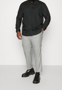 Zwart overhemd met knopen en een gestructureerde kraag, gecombineerd met lichtgrijze geruite broek en zwarte veterschoenen.