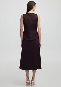 Sleeveless, dark purple top with a smooth texture and back zipper, paired with a matching long skirt, also in similar fabric.