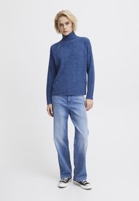 Sinine, ribaga kudum, kõrge kaelusega ja poole tõmblukuga, koos helesiniste sirgete säärtega teksade ja mustade spordijalatsitega.