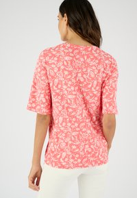 Blusa de estampado floral coral con mangas cortas, escote redondo y patrones blancos de hojas y flores. Tejido suave con un corte relajado.