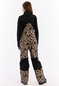 Bavaglini a fantasia leopardata con dettagli neri, dotati di spalline regolabili, vestibilità comoda e materiale resistente. Camicia nera a maniche lunghe sotto.