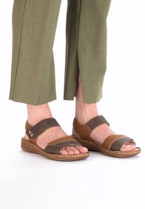 Sandales en cuir marron avec de larges brides. Le design présente un schéma de couleurs marron et gris, des orteils ouverts et une semelle basse et texturée.